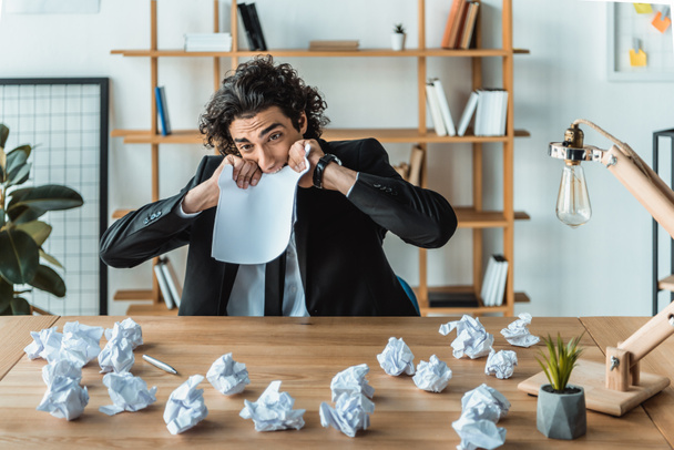 hombre de negocios mordiendo papel en el lugar de trabajo
 - Foto, Imagen