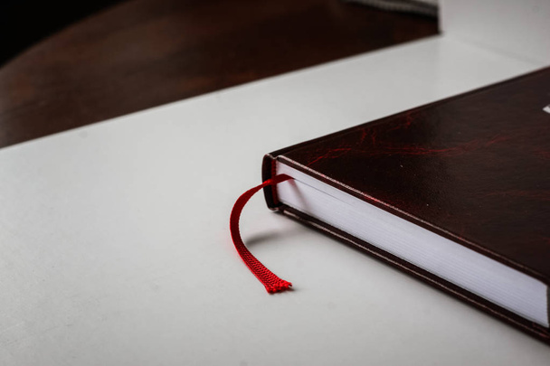 A beautiful closeup of a book in dark red cover and with red bookmark. Shallow depth of field - Фото, зображення