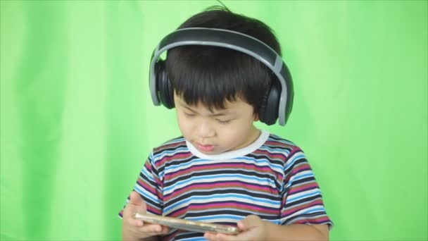 carino asiatico bambino in piedi in il studio mentre ascoltare musica su la sua smartphone con auricolare
. - Filmati, video