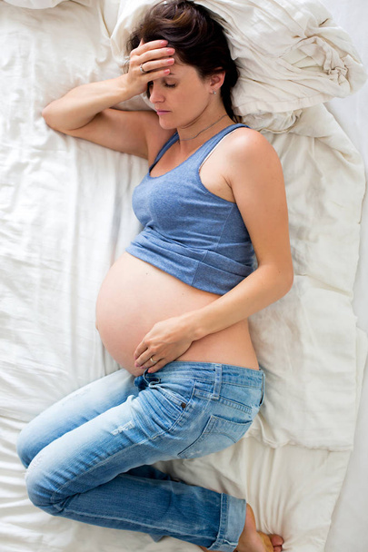 Young pregnant woman lying in bed with pain - Foto, Bild