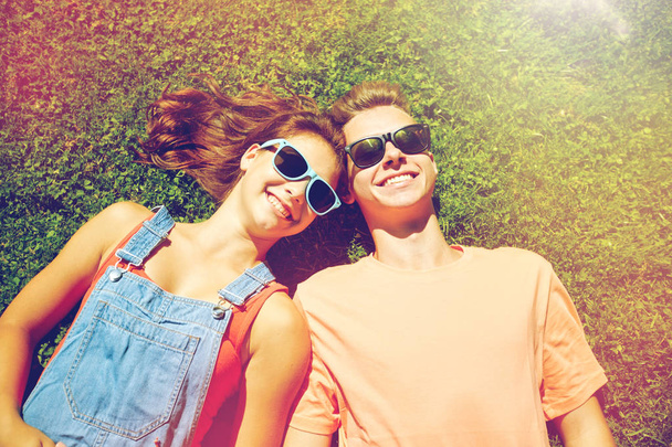 happy teenage couple lying on grass at summer - Фото, изображение