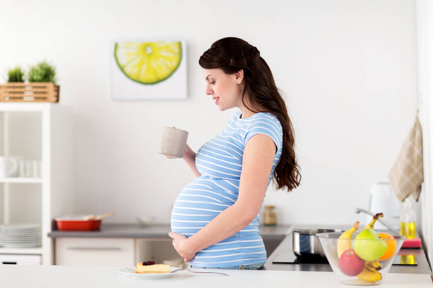 happy pregnant woman with mug and cake at home - Foto, Bild