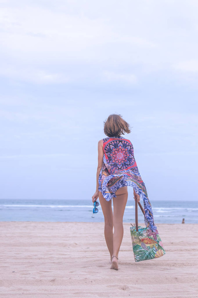 Turista mujer caminando en una playa tropical de vacaciones de verano con gafas de sol y bolsa de playa relajante en vacaciones de viaje. Jovencita en ropa de playa de moda de lujo, isla de Bali, Indonesia
. - Foto, Imagen