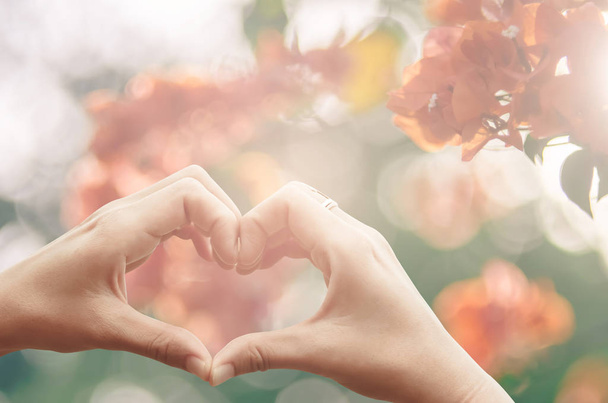Női kezek szív forma, a természet rózsaszín bokeh sun light fáklyát, és virág absztrakt textúra háttér életlenítés. Boldog szerelem és a szabadság fogalmát. Vintage hang szűrő color stílus. - Fotó, kép