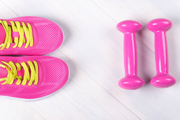 Pink set of dumbbells and sneakers on a wooden gray background - Foto, Bild