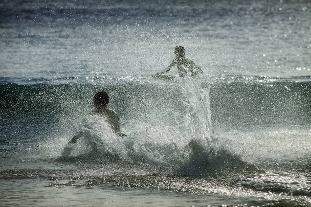 Siluetas de personas en las salpicaduras del océano al atardecer
 - Foto, imagen