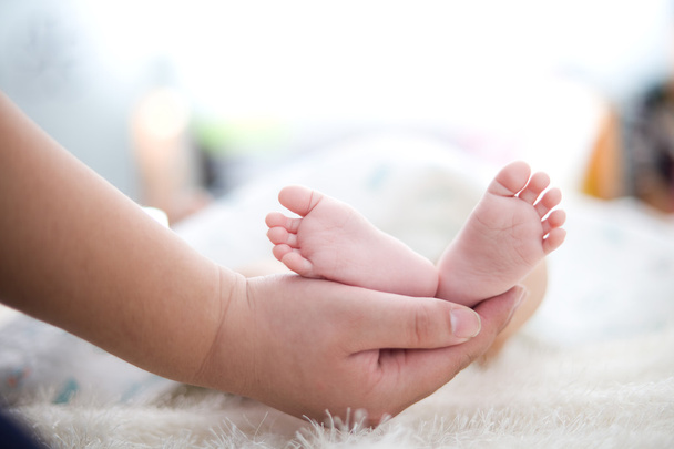 Mão da mãe segura o pé do bebê
 - Foto, Imagem