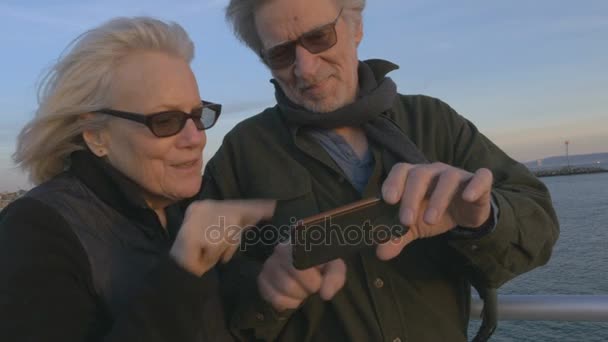 Aantrekkelijk gelukkig lachend ouder paar in 60s gebruikend smartphone bij zonsondergang - Video