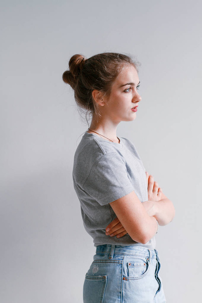 A beautiful, sweet girl in jeans and a sweatshirt stands near a white wall - Foto, afbeelding
