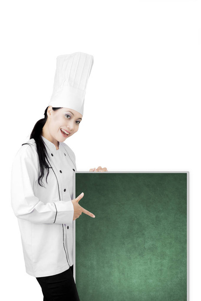 Beautiful chef pointing a blank chalkboard - Фото, изображение