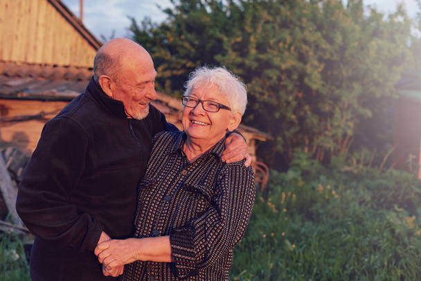 Authentic outdoor shot of aging couple having fun in the garden and blessed with love. During their game man is trying to kiss his partner and she is laughing out loud. Love and family concept. - Photo, Image