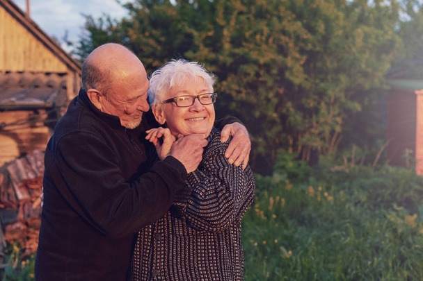 Настоящий наружный снимок стареющей пары, развлекающейся в саду и благословенной любовью. Во время их игры человек пытается поцеловать своего партнера, и она смеется вслух. Концепция любви и семьи. - Фото, изображение