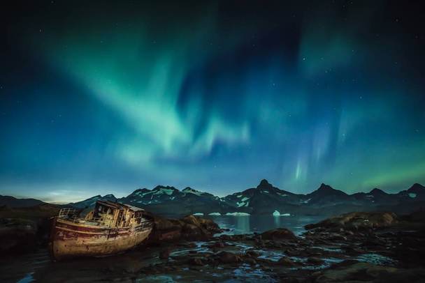 Aurora au-dessus des montagnes du Groenland avec bateau de pêche abandonné au premier plan
 - Photo, image
