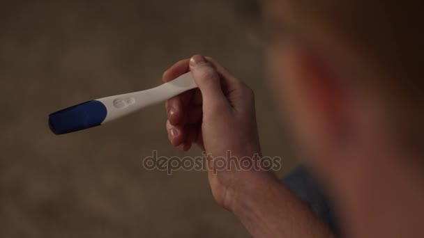 Man looks at a pregnancy test side view. Positive pregnancy test held by a surprised man. Guy holding pregnancy test back view - Footage, Video