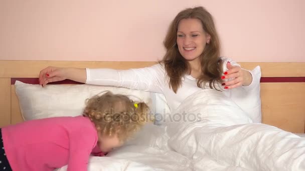 Непослушная маленькая девочка легла в постель и обняла свою мать. Веселые семейные девушки развлекаются
 - Кадры, видео