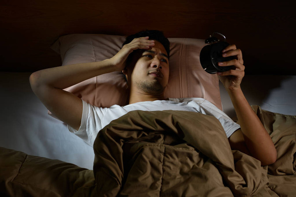 Przygnębiony człowiek cierpi na bezsenność, patrząc na budzik, leżąc w łóżku - Zdjęcie, obraz