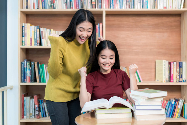 Dos estudiantes asiáticos leyendo libros en la biblioteca universitaria y
 - Foto, Imagen