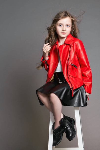 Fashion Girl in a red jacket poses and grimaces and makes a face. Photo Studio on a gray background. Birthday, holiday - Foto, Imagem