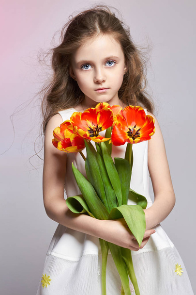 Fashion red-haired girl with tulips in hands. Studio photo on light coloured background. Birthday, holiday, mother's day, first day of school - Photo, image