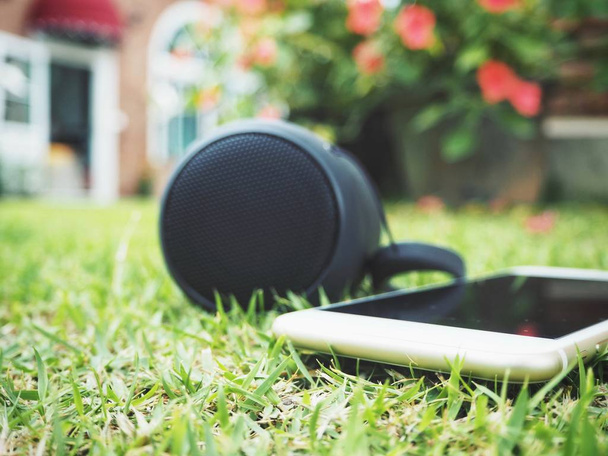 Nahaufnahme von Bluetooth-Lautsprecher mit Smartphone auf grünem Gras - Foto, Bild
