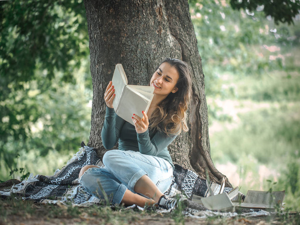 a young girl near a tree reading a book - Foto, Imagen