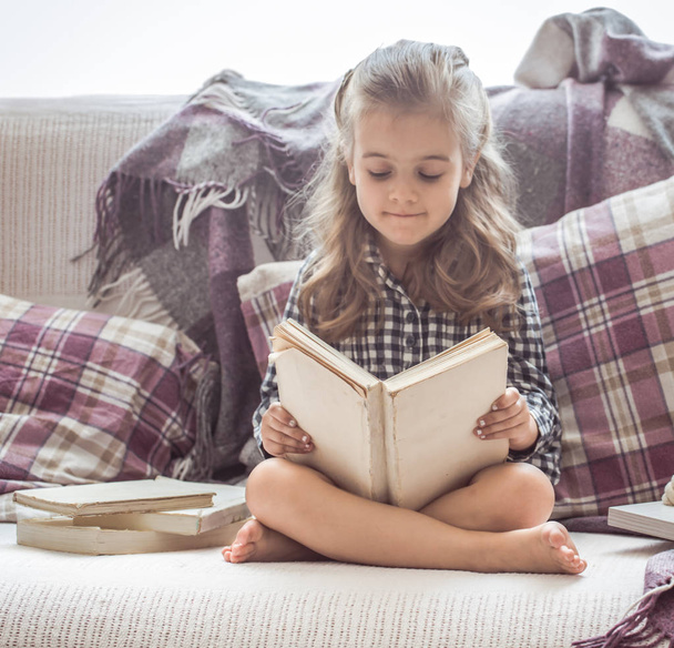 Mała dziewczynka czytanie książki na kanapie - Zdjęcie, obraz