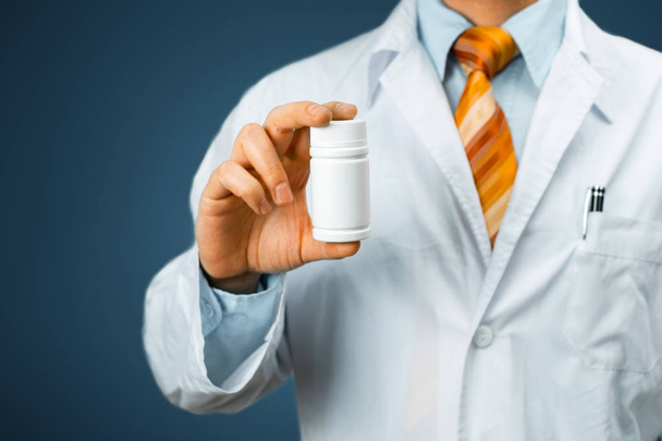 Hombre Doctor en capa blanca con un estetoscopio en el hombro sosteniendo una botella de pastillas entre los dedos. Concepto de Hospital Médico de Salud
 - Foto, imagen