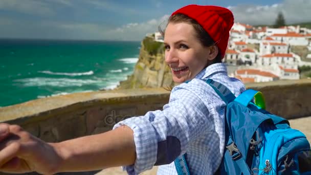 Sígueme - mujer joven feliz con un sombrero rojo y con una mochila detrás de su espalda tirando de chicos mano en Azenhas do Mar, Portugal. Caminando de la mano a la costa del océano
 - Imágenes, Vídeo