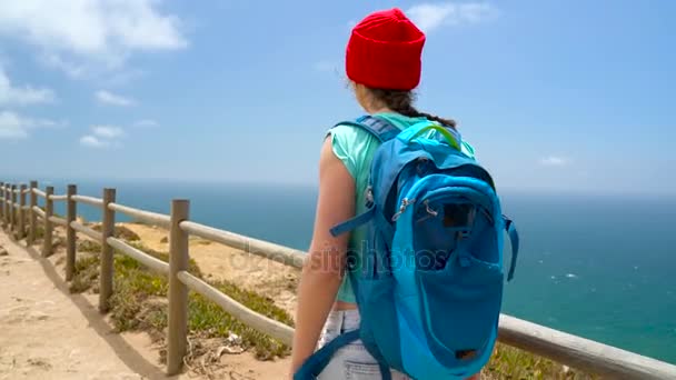 Mulher com uma mochila vai em um terreno montanhoso pitoresco para o oceano
 - Filmagem, Vídeo