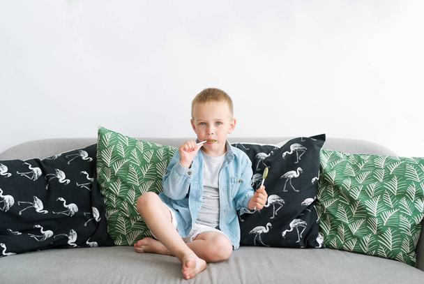 Small boy sitting with lollipop on coach in living room at home - Photo, Image