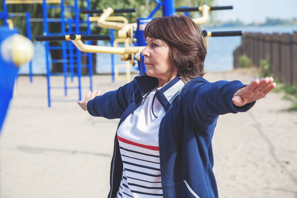 Cute retired woman performs gymnastic exercises on street - Foto, Imagen