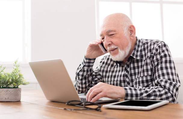 Vanhempi mies puhuu puhelimessa kannettavan tietokoneen kanssa
 - Valokuva, kuva