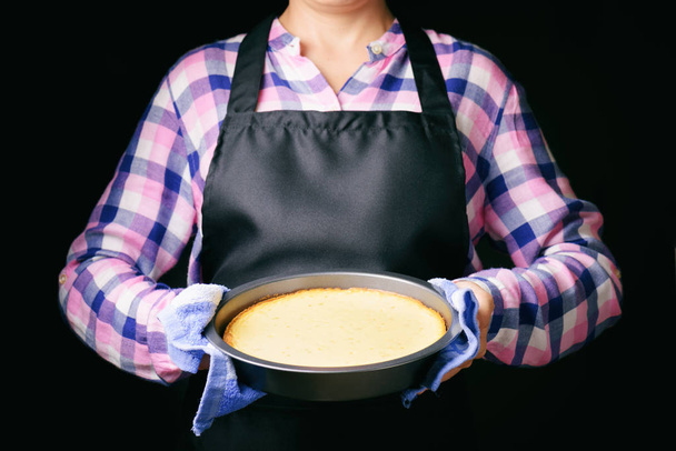 Freshly baked cheesecake in hands on black apron background - 写真・画像