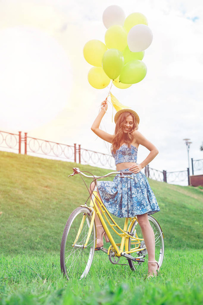Happy girl posing on yellow bicycle with ballons and smiling. - Zdjęcie, obraz