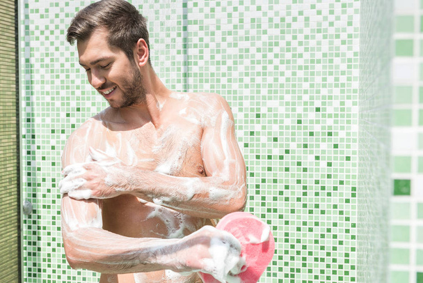 Happy young bearded guy cleaning body in bathroom - Foto, Imagem