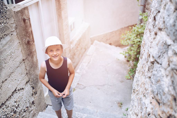 Kind mit weißem Hut spaziert durch enge Gasse der Altstadt - Foto, Bild