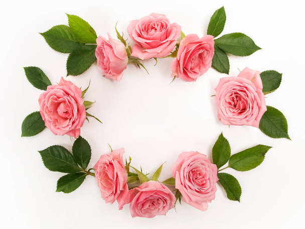 Round frame made of pink roses, green leaves, branches, floral pattern on white background. Flat lay, top view. - Foto, imagen
