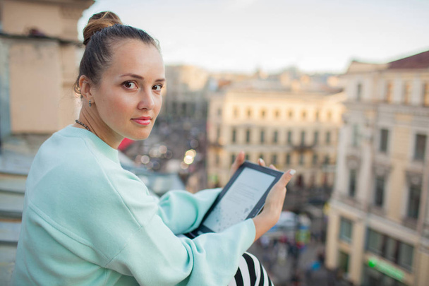 attraktives und stilvolles Mädchen sitzt auf dem Dach des Hauses in der Altstadt und liest das E-Book - Foto, Bild
