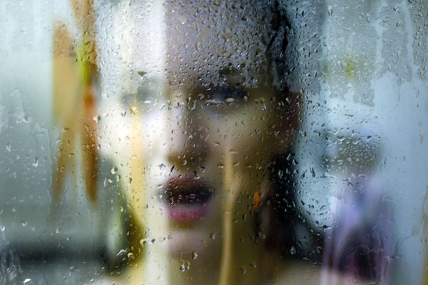Krásná žena za sklem s kapkami vody se dívá přímo do kamery. Dívka se sprchuje, voyérství - Fotografie, Obrázek
