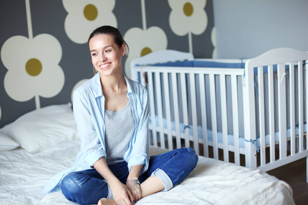 Young woman sitting on the bed near childrens cot. Young mom - Φωτογραφία, εικόνα