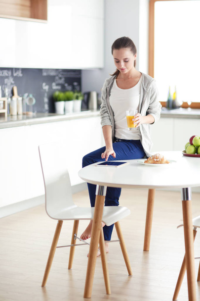 Young woman with orange juice and tablet in kitchen. - Photo, Image