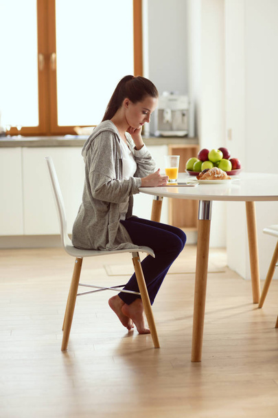 Young woman with orange juice and tablet in kitchen. - Foto, afbeelding