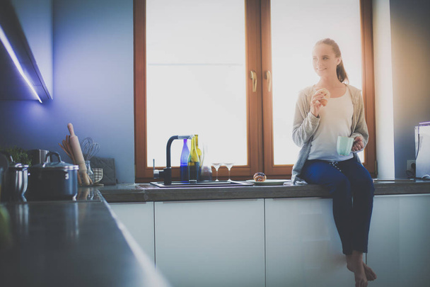 Beautiful young woman using a digital tablet in the kitchen. - 写真・画像