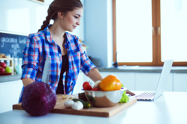 Young woman cutting vegetables in kitchen near desk. - Valokuva, kuva