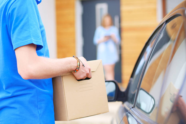 Usmívající se doručovatel v modré uniformě doručující balíček příjemci - koncept kurýrní služby. Usmívající se doručovatel v modré uniformě - Fotografie, Obrázek