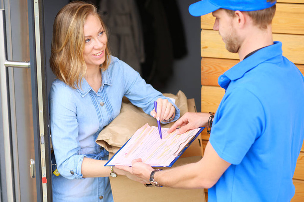 Smiling delivery man in blue uniform delivering parcel box to recipient - courier service concept. Smiling delivery man in blue uniform - 写真・画像
