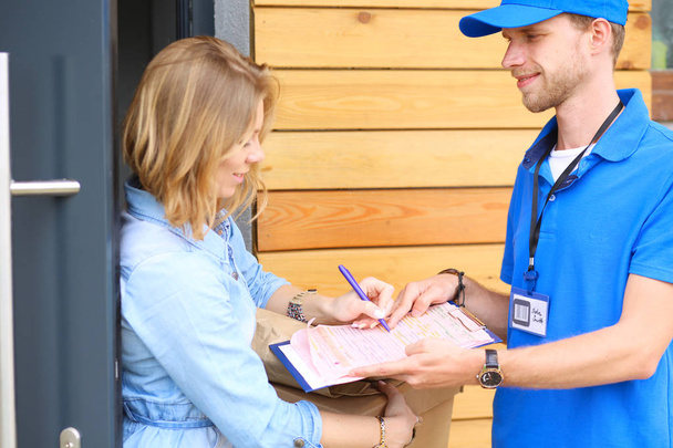 Smiling delivery man in blue uniform delivering parcel box to recipient - courier service concept. Smiling delivery man in blue uniform - Zdjęcie, obraz