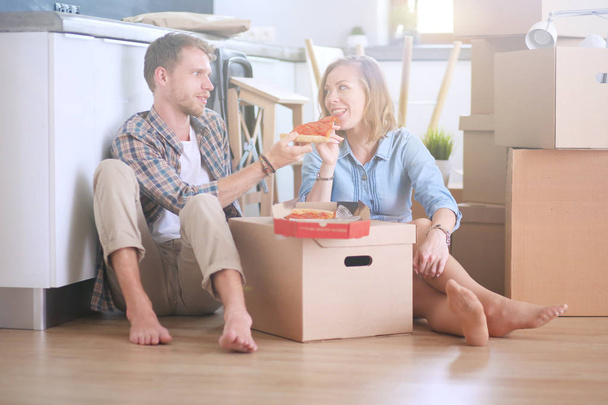 Young couple have a pizza lunch break on the floor after moving into a new home with boxes around them. Young couple - Valokuva, kuva