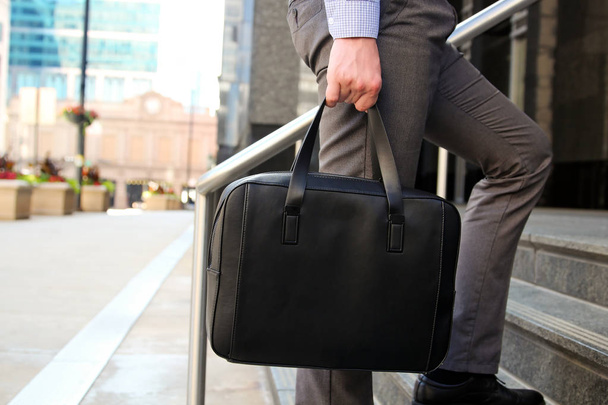 Businessman walking and holding  a  leather briefcase in his handss Modern city behind  - Foto, Imagem