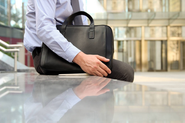 Geschäftsmann sitzt / ruht nach dem Arbeitstag und hält eine lederne Aktentasche in der Hand - Foto, Bild
